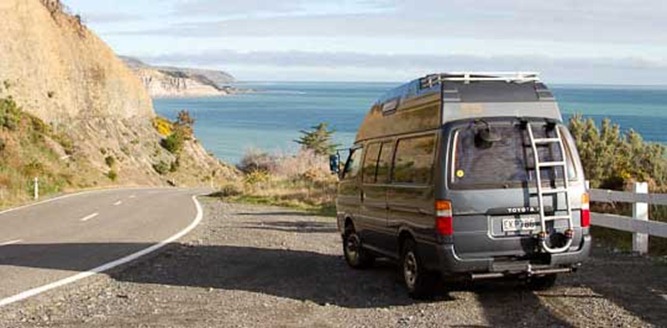 A campervan parked on a coastal road above the ocean, South Island, New Zealand